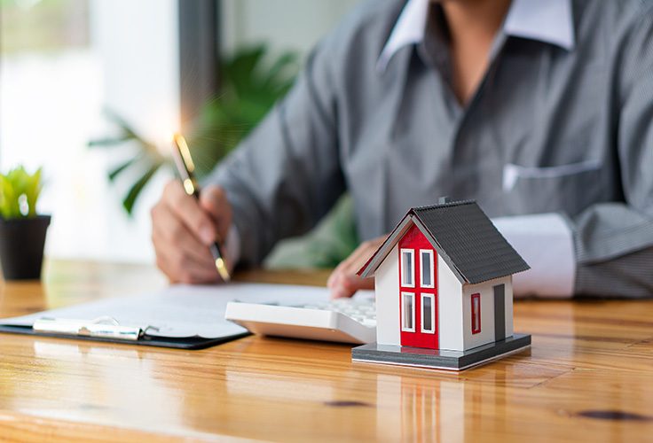 Immobilienmakler bei der Immobilienbewertung mit Taschenrechner neben Hausmodell