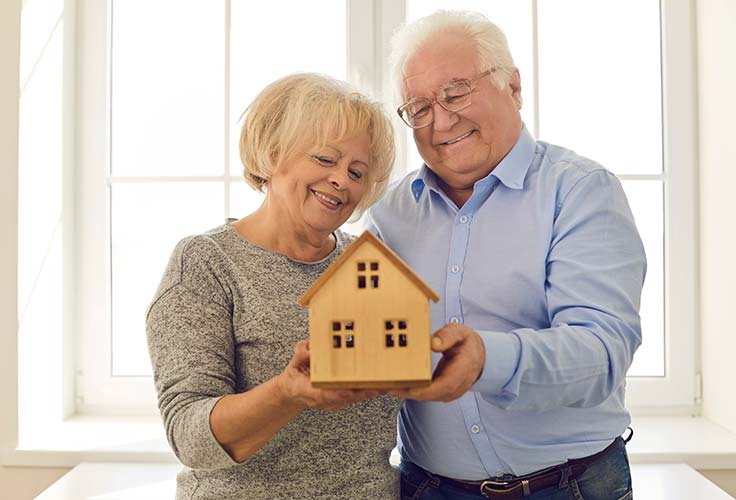 Älteres Ehepaar mit einem Modellhaus in den Händen denkt über die Immobilienverrentung nach