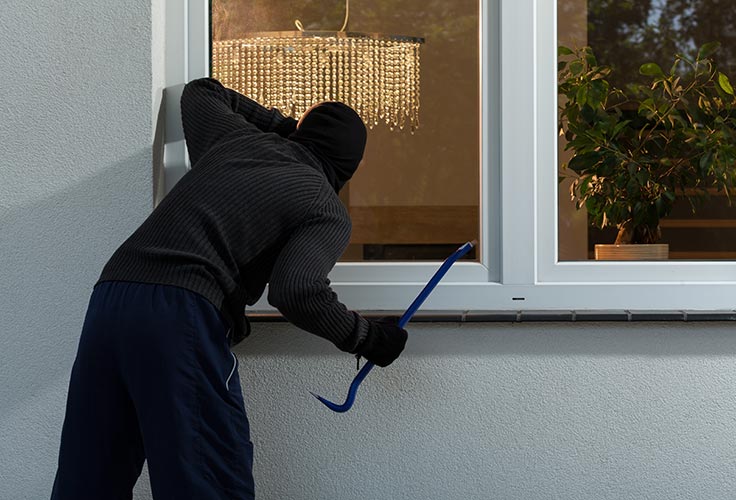 Einbrecher mit Eisenstange blickt in ein Fenster